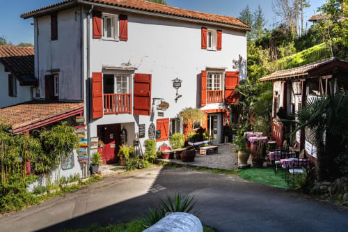 Entrée du Moulin de Pascale chambre d'hôtes à Espelette avec ses volets rouges typiques et sa terrasse de restaurant accueillante.