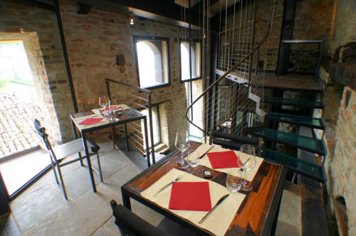 Sala da pranzo di Dimora i Manichei con mattoni a vista, tavolo moderno con accenti rossi, scala a spirale a Monforte d'Alba