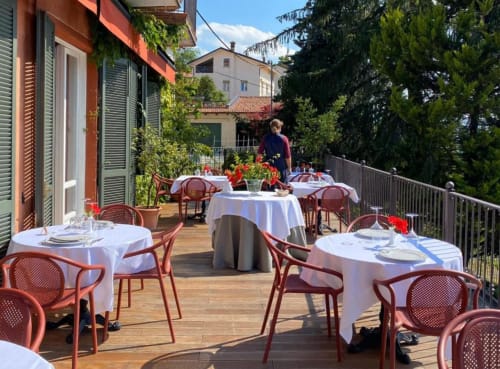 Terrazza esterna per cena a Dimora i Manichei a Monforte d'Alba con tavoli apparecchiati, sedie rosse e vista sulla campagna toscana.