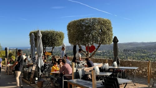 Une des nombreuses terrasses de café et de restaurant, sur Les Remparts Ouest, offrant une vue sur la vallée, la Méditerranée et le Cap d’Antibes, très agréable pour les couchers de soleil
