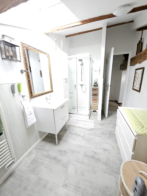 Modernes Badezimmer im Manoir Lacustre mit weißem Waschtisch, vergoldetem Spiegel, offener Dusche und sichtbaren Holzbalken