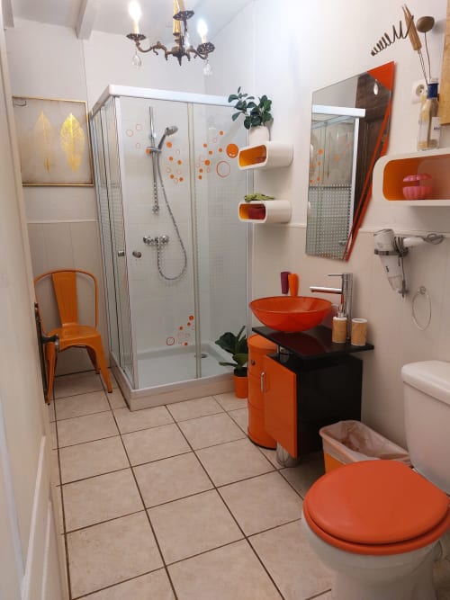 Modernes Badezimmer mit orangefarbenen Akzenten, Aufsatzwaschbecken, Duschbereich und Pflanzen im Manoir Lacustre B&B in Queyrac