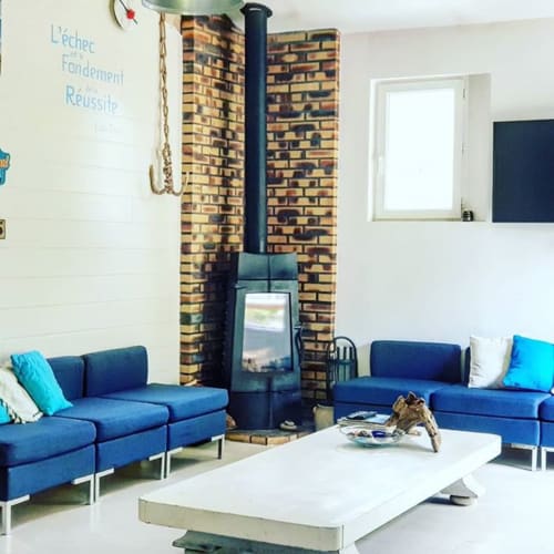 Modernes Lounge mit blauem modularem Mobiliar, Ziegelfeuerstelle und weißen Tischen im Le Manoir Lacustre, Queyrac