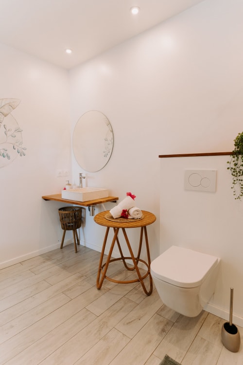 Salle de bains moderne à l'Habitation I'SEO à Sainte-Anne avec lavabo vasque, miroir rond, table en bois et toilettes blanches