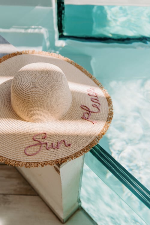 Straw sun hat with 'Sun & sand' embroidered text by turquoise pool at Habitation I'SEO, Sainte-Anne