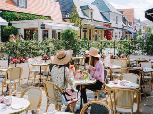 Outdoor café seating at Residence Disneyland Place Toscane in Serris with diners enjoying the terrace amid flowering gardens
