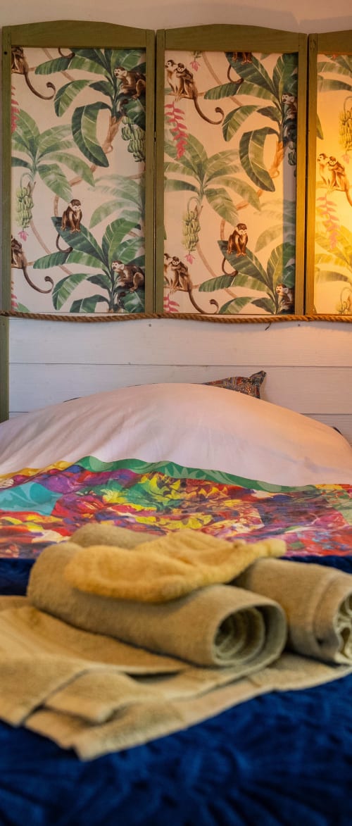 Détail cosy de la chambre Guéthary : paravent tropical, linge de lit coloré et serviettes accueillantes pour un séjour relaxant.