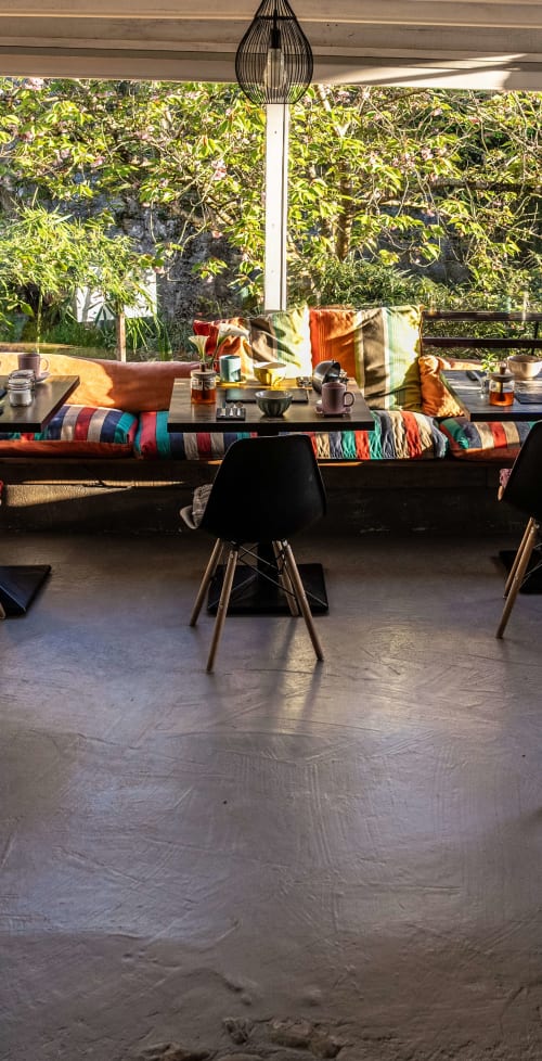 Salle de petit-déjeuner lumineuse ouverte sur la nature, banquettes aux couleurs basques et ambiance sereine au bord de l'eau.
