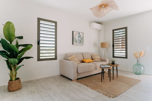 Salon moderne à l'Habitation I'SEO à Sainte-Anne avec canapé beige, plantes tropicales et lumière naturelle des jalousies