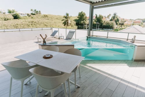 Terrasse panoramique avec piscine turquoise, table à manger, chaises longues et vue sur les collines à Habitation l'SEO à Sainte-Anne,