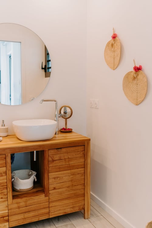 Vanité moderne avec lavabo blanc rond, meuble en bois, miroir circulaire et décoration en rotin à Sainte-Anne