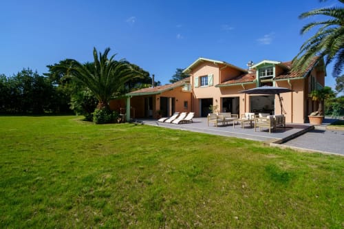 Villa color durazno con palmeras, césped verde y zona de estar en La Conciergerie Biarritz