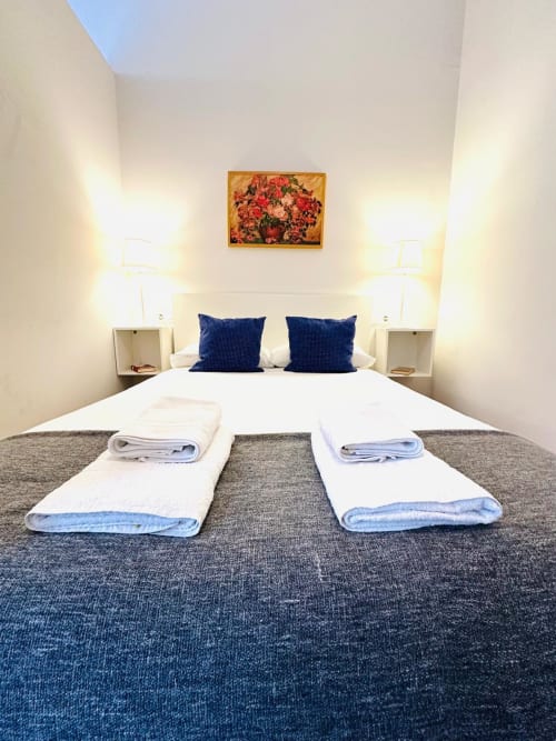 Moderno dormitorio en Mérida con dos camas, almohadas azules, mesitas blancas, lámparas y arte floral sobre cabecera.