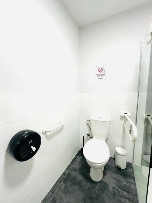 Baño limpio con azulejos blancos, inodoro, dispensador de papel y barras de seguridad en el apartamento Gestyp-AT en Mérida
