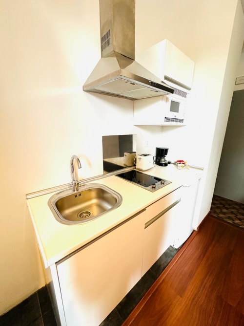 Cocina compacta en apartamento de Mérida con fregadero de acero inoxidable, estufa, campana extractora y gabinetes blancos