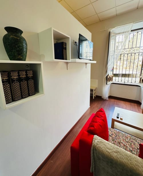 Moderno salón de apartamento en Mérida con estanterías blancas, sofá rojo, pisos de madera y vistas a puntos de interés desde las ventanas