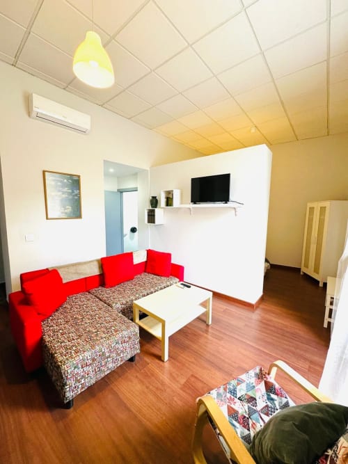 Sala de estar moderna en Mérida con sofá rojo, pisos de madera, televisor de pantalla plana e iluminación de techo brillante