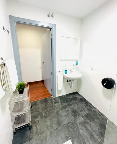 Baño moderno en apartamento Gestyp-AT, Mérida con paredes blancas, piso de baldosas grises, lavamanos, espejo y soluciones de almacenamiento.