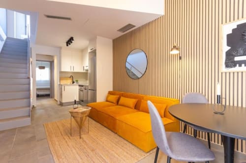 Salón moderno en los Apartamentos J&A de Terrassa con sofá naranja, mesa de comedor y pared de acento con listones de madera.
