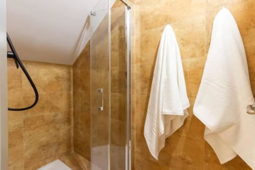Baño moderno en J&A Apartments Terrassa con ducha de azulejos dorados, mampara de vidrio y toallas blancas