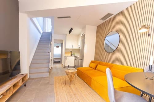 Estudio moderno J&A Apartments en Terrassa con sofá amarillo, cocina abierta, suelos de madera y escalera