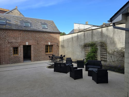 Cour du Gîte Les Mouettes Blessées au Crotoy avec salon de jardin noir, petite maison en briques et murs en pierre sous un ciel dégagé