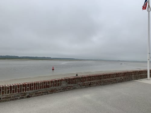 Mur de briques rouges en bord de mer du Gîte Les Mouettes Blessées au Crotoy, avec vue sur la baie nuageuse et drapeau français