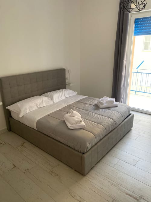 Camera moderna presso l'hotel La Maison Srls a Bari con letto grigio imbottito, biancheria bianca e balcone con vista sulla città
