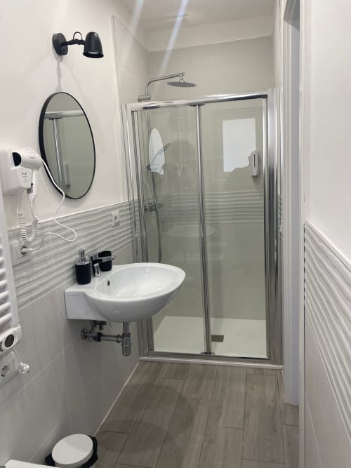 Bagno moderno presso l'hotel La Maison a Bari con doccia walk-in, specchio rotondo e lavabo bianco su piedistallo