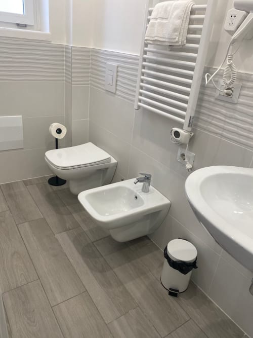 Bagno moderno presso La Maison Srls a Bari con sanitari bianchi, scaldasalviette e pavimentazione in effetto legno