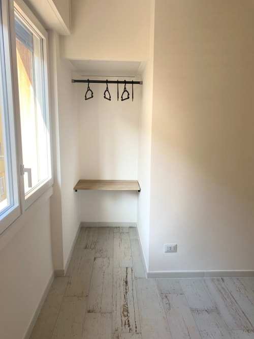 Angolo guardaroba minimalista con ripiano in legno, sbarra per trazioni nera e ganci presso l'hotel La Maison Srls a Bari, Italia