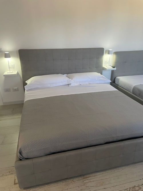 Camera moderna presso La Maison Srls a Bari con letto imbottito grigio, cuscini bianchi e letti gemelli visibili