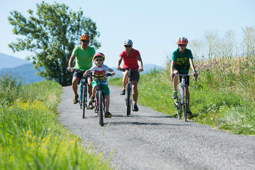 Familia en bicicleta en un camino rural cerca de Béziers con montañas y campiña verde de fondo