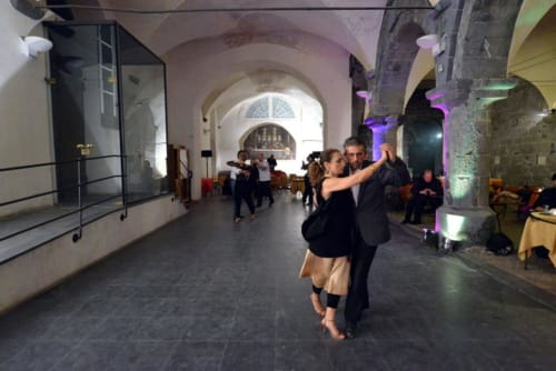 Coppia che balla nella storica sala in pietra con volta ad arco di CasaRosada illuminata da luci viola a Vidracco