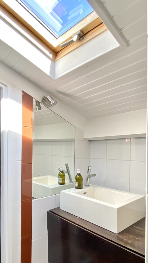 Salle de bains moderne de la VillaSerenita à Ajaccio, Corse, France avec puits de lumière, vasque blanche, miroir et meuble en bois sombre