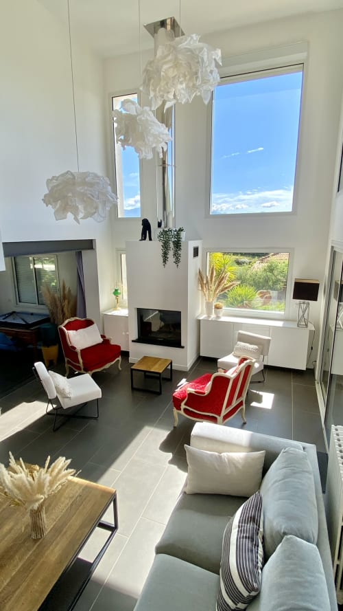 Élégant salon de la VillaSerenita à Ajaccio, Corse, France avec fauteuils en velours rouge, cheminée et baies vitrées panoramiques donnant sur le jardin.