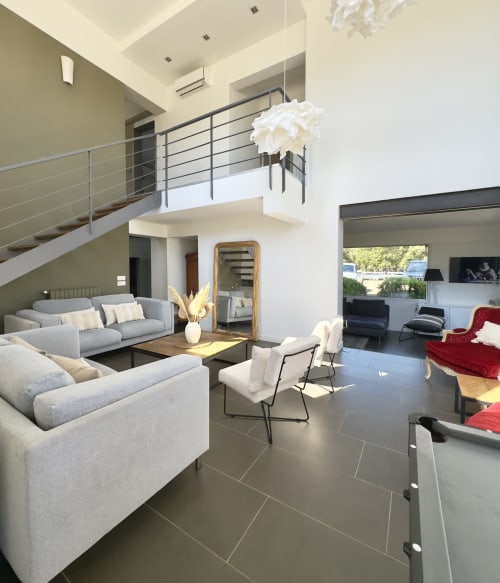 Salon double hauteur moderne de la VillaSerenita à Ajaccio, Corse, France avec canapés gris, sièges en velours rouge et mezzanine