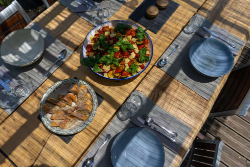 Outdoor dining table at Maison Mûrier in Fayssac with colorful salad, sliced bread, blue plates, and place settings in bright