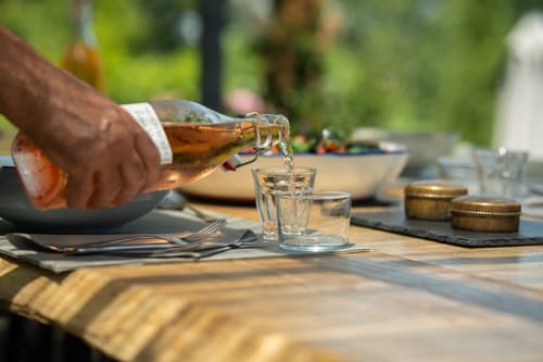 Hand pouring rosé wine at outdoor dining table, Maison Mûrier B&B in Fayssac
