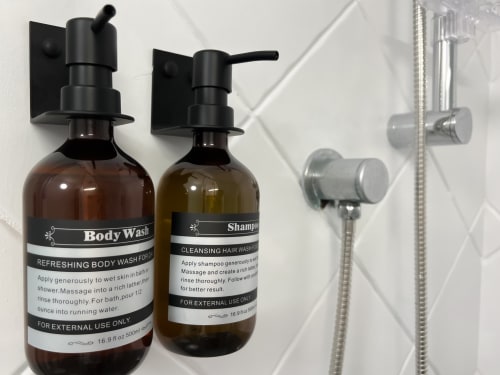 Distributeurs de gel douche et shampoing fixés au mur de carrelage blanc dans la salle de bain de CefalHome Roma