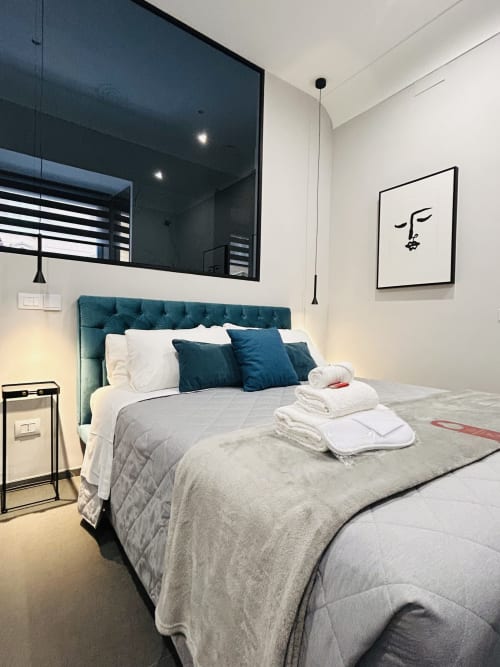 Modern guest room at AD Trastevere with teal upholstered bed, white bedding, minimalist line art, and ensuite bathroom in