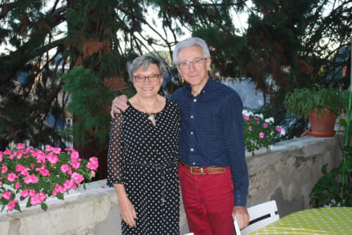 Two guests smiling together in Le Fassardy's garden courtyard in Châteauroux, surrounded by pink flowers and greenery.