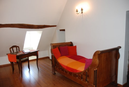 Charming attic bedroom at Le Fassardy B&B in Châteauroux with wooden beams, colorful bedding, and vintage furnishings