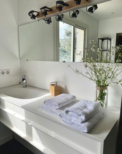 Vasque moderne de la VillaSerenita Ajaccio avec lavabo blanc, serviettes pliées, fleurs fraîches et éclairage du miroir