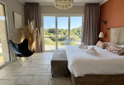 Chambre moderne de la VillaSerenita Ajaccio avec lit king size, mur d'accent orange et baies vitrées panoramiques sur les jardins