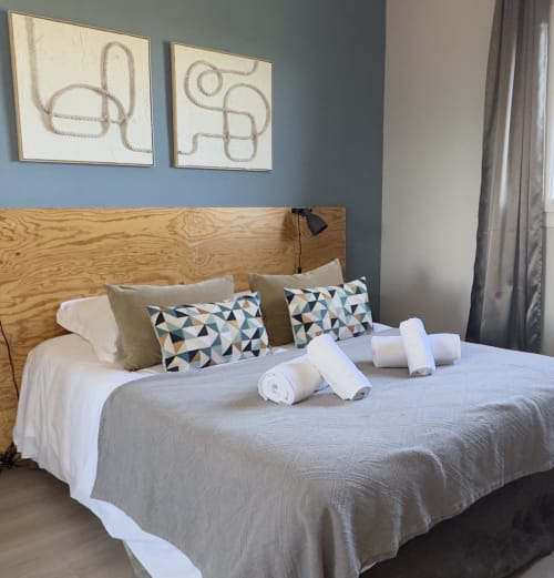 Chambre à VillaSerenita Alata avec tête de lit en bois, coussins géométriques et serviettes roulées sur le lit