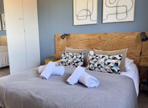 Chambre moderne de la VillaSerenita Alata avec lit en bois, coussins géométriques, serviettes roulées et murs bleus