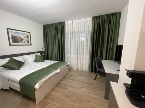 Camera dell'Hotel Saint Michel a Gorizia con letto matrimoniale, dettagli verdi, scrivania e balcone con vista sulla città