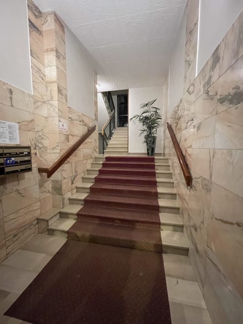 Scala moderna con moquette bordeaux dell'Hotel Saint Michel a Gorizia, con pareti in marmo e ringhiere in legno