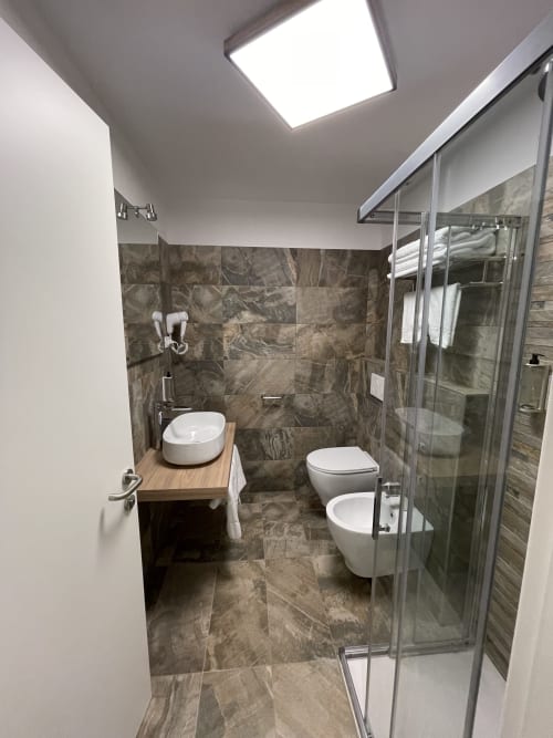 Bagno moderno dell'Hotel Saint Michel Gorizia con piastrelle in marmo, doccia, lavabo e wc
